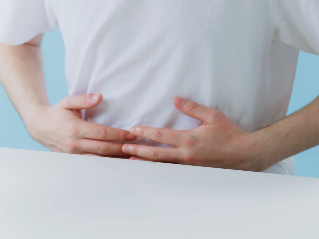 A man in a white T-shirt holding his stomach in pain